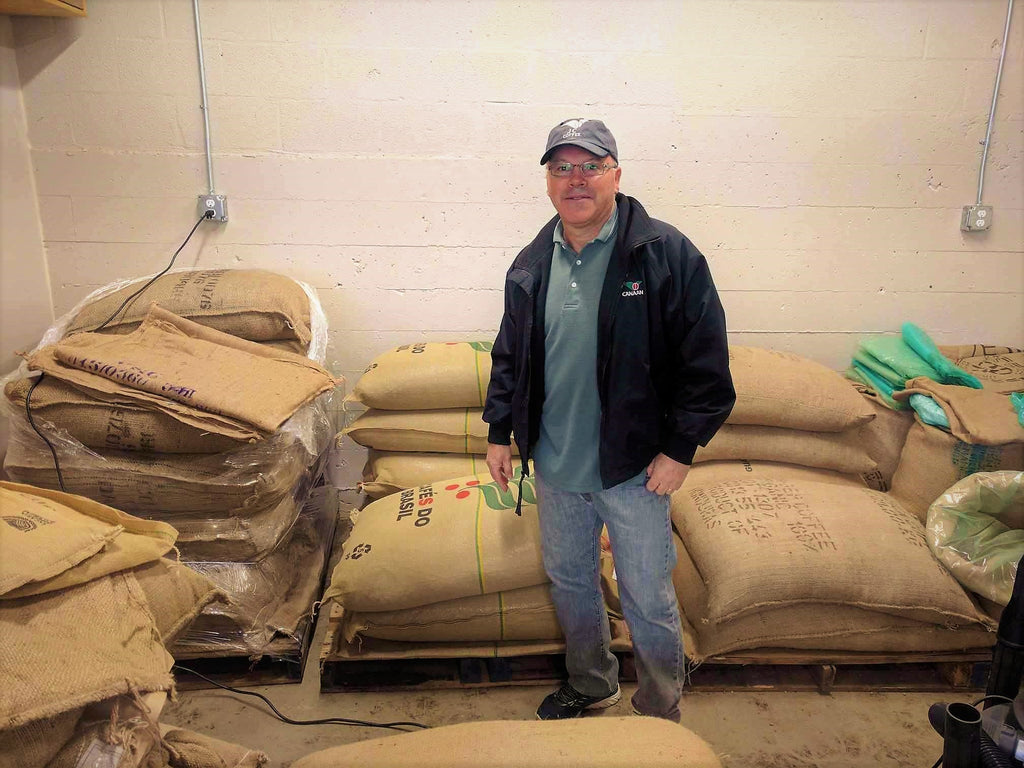 Sérgio Dias standing among bags of green coffee at a Seattle roastery